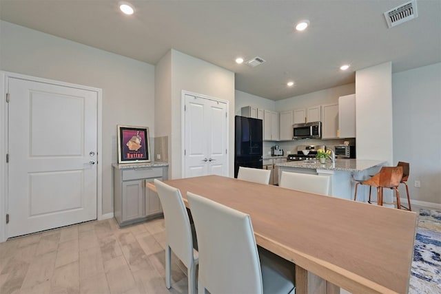 kitchen featuring gray cabinetry, a breakfast bar, light hardwood / wood-style flooring, appliances with stainless steel finishes, and kitchen peninsula