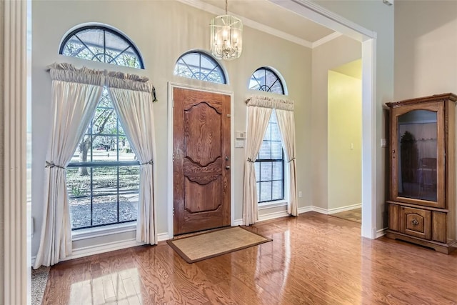 foyer entrance with wood-type flooring, an inviting chandelier, plenty of natural light, and crown molding