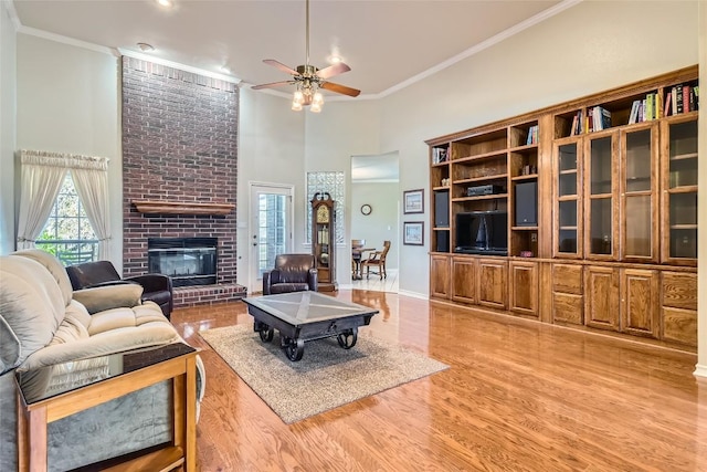 living room with hardwood / wood-style floors, a brick fireplace, ceiling fan, a towering ceiling, and ornamental molding