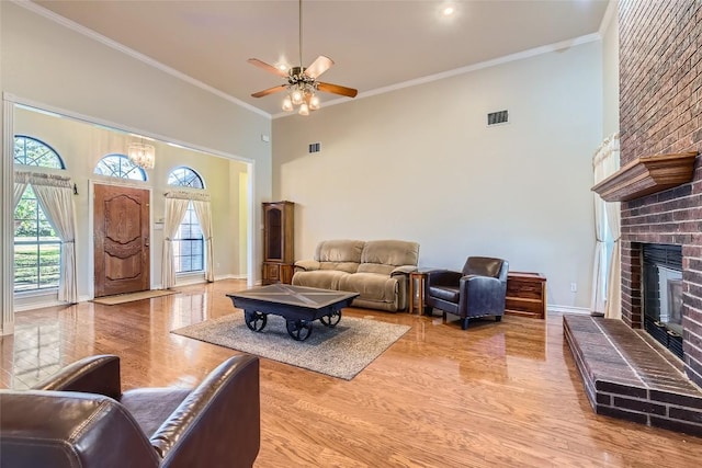 living room featuring ceiling fan, crown molding, a towering ceiling, and a fireplace