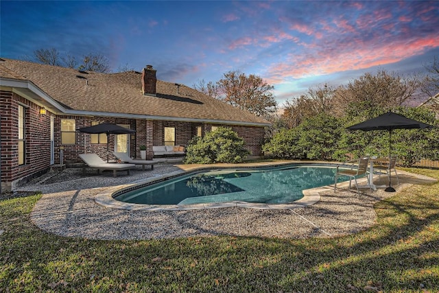 pool at dusk with outdoor lounge area, a yard, and a patio area