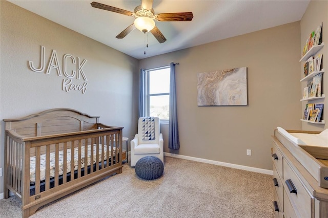 bedroom featuring ceiling fan, light colored carpet, and a nursery area