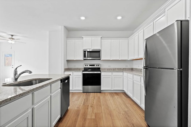 kitchen with sink, white cabinetry, light hardwood / wood-style flooring, light stone countertops, and appliances with stainless steel finishes