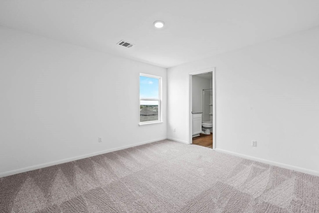 unfurnished bedroom with ensuite bathroom and dark colored carpet