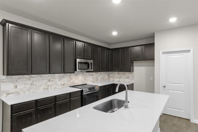 kitchen featuring sink, tasteful backsplash, appliances with stainless steel finishes, hardwood / wood-style flooring, and a kitchen island with sink