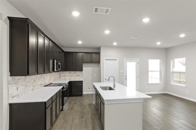 kitchen featuring sink, appliances with stainless steel finishes, an island with sink, hardwood / wood-style flooring, and backsplash