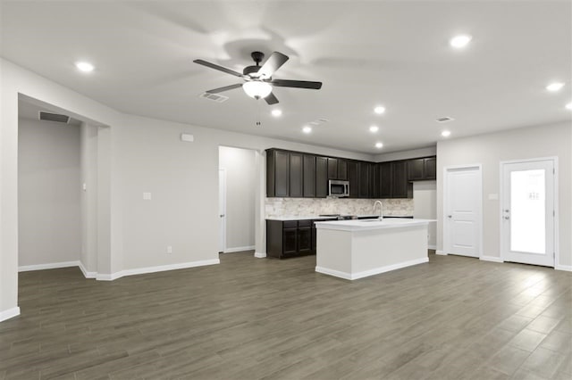 kitchen with tasteful backsplash, an island with sink, ceiling fan, and dark hardwood / wood-style flooring