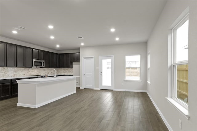 kitchen featuring dark hardwood / wood-style floors, a kitchen island with sink, and decorative backsplash