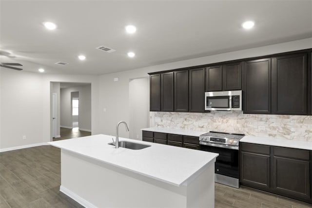 kitchen with sink, hardwood / wood-style flooring, appliances with stainless steel finishes, backsplash, and a center island with sink