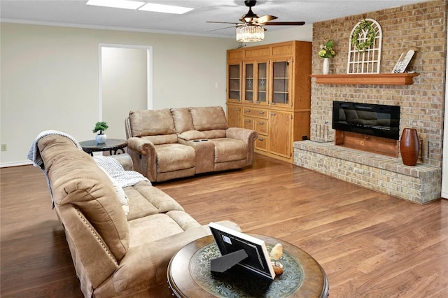 living room with ceiling fan, wood-type flooring, crown molding, and a brick fireplace