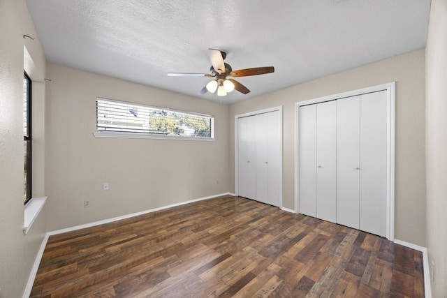 unfurnished bedroom with a textured ceiling, two closets, ceiling fan, and dark wood-type flooring