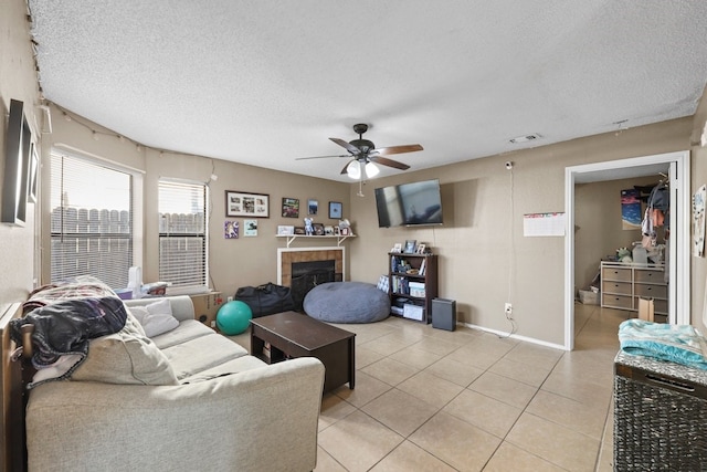 tiled living room featuring ceiling fan, a fireplace, and a textured ceiling