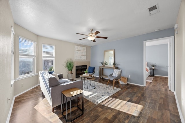 living room featuring ceiling fan, dark hardwood / wood-style flooring, and a tiled fireplace