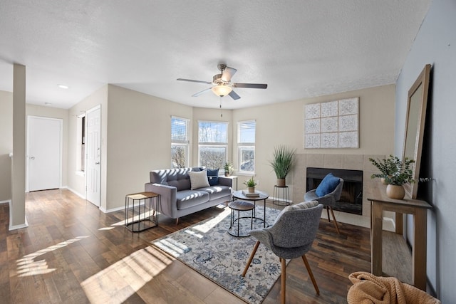 living room featuring a fireplace, a textured ceiling, ceiling fan, and dark wood-type flooring