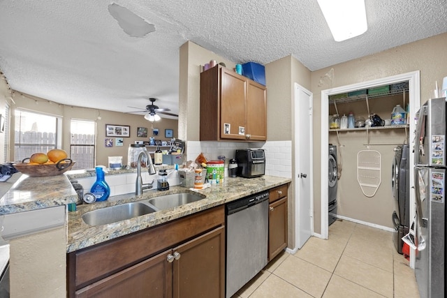 kitchen with a textured ceiling, stainless steel appliances, ceiling fan, sink, and washing machine and clothes dryer