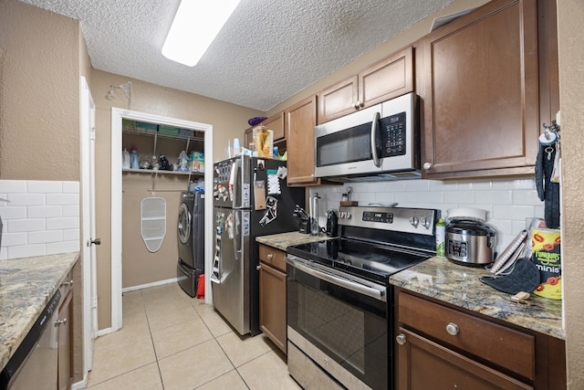 kitchen featuring washer and dryer, light tile patterned floors, appliances with stainless steel finishes, tasteful backsplash, and light stone counters