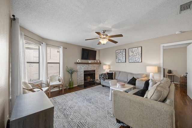 living room featuring ceiling fan, a fireplace, wood-type flooring, and a textured ceiling