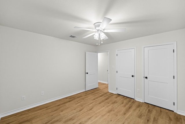 unfurnished bedroom featuring multiple closets, ceiling fan, and light wood-type flooring