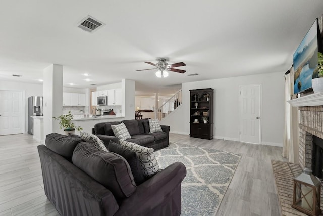 living room with ceiling fan, a fireplace, and light wood-type flooring