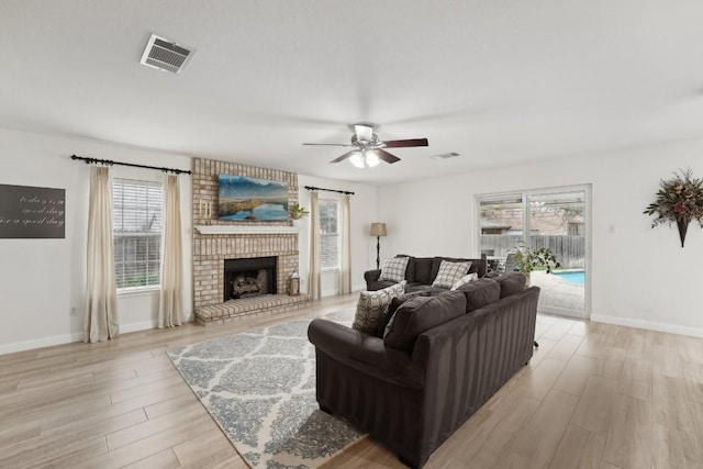 living room featuring ceiling fan, a healthy amount of sunlight, light wood-type flooring, and a fireplace