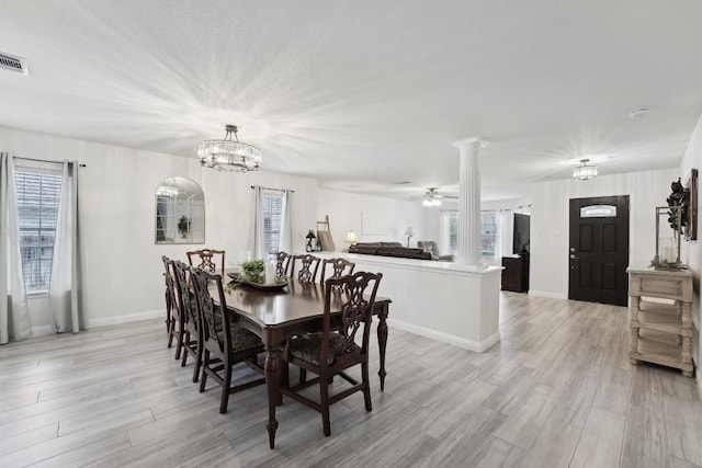 dining room with ceiling fan with notable chandelier, light wood-type flooring, and decorative columns