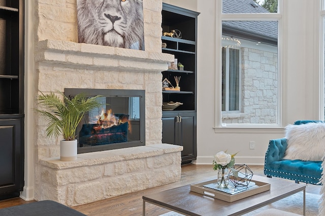 living room with built in shelves, a stone fireplace, and wood-type flooring