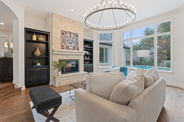 living room with built in shelves, crown molding, a stone fireplace, and wood-type flooring