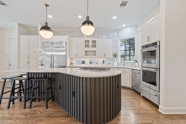 kitchen featuring a large island, hanging light fixtures, stainless steel appliances, white cabinets, and light wood-type flooring