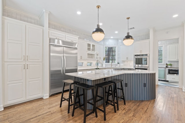 kitchen featuring white cabinetry, light hardwood / wood-style flooring, pendant lighting, a spacious island, and appliances with stainless steel finishes