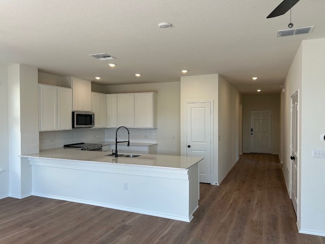 kitchen featuring visible vents, a peninsula, stainless steel appliances, white cabinetry, and a sink