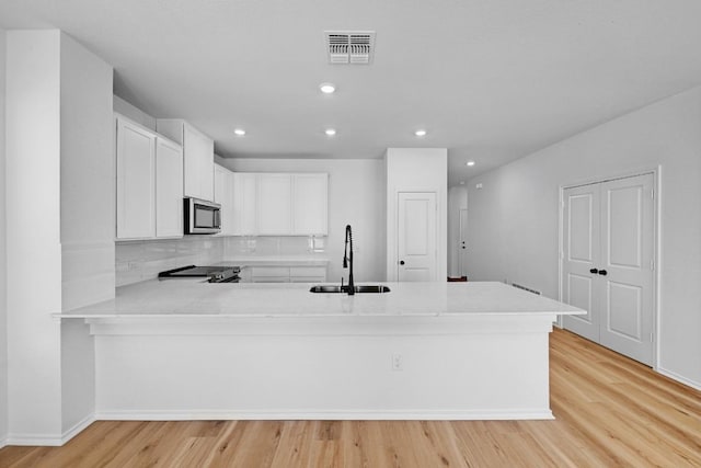 kitchen with light wood-type flooring, light countertops, appliances with stainless steel finishes, a peninsula, and a sink