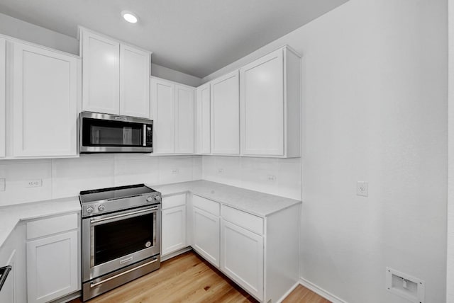 kitchen featuring decorative backsplash, light countertops, appliances with stainless steel finishes, white cabinetry, and light wood-type flooring