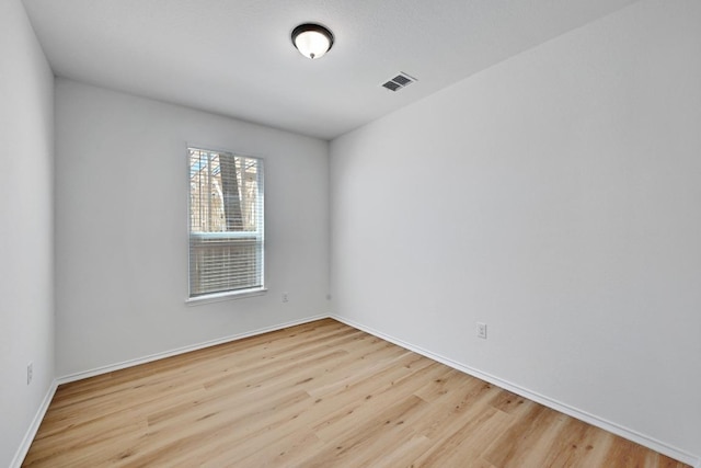 empty room with wood finished floors, visible vents, and baseboards