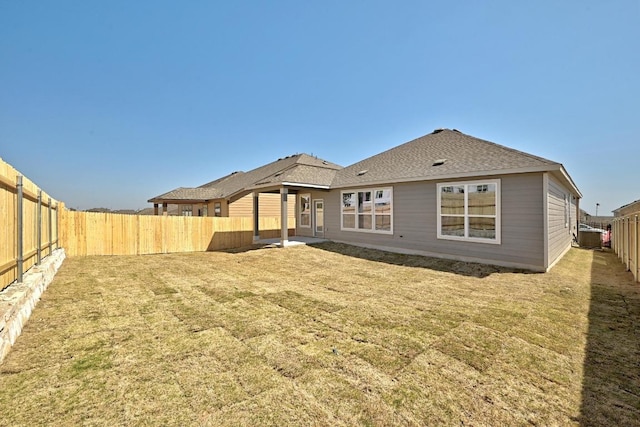 rear view of property with a lawn, a fenced backyard, and roof with shingles