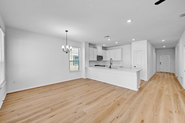 kitchen featuring stainless steel microwave, light wood-style flooring, a peninsula, white cabinetry, and a sink