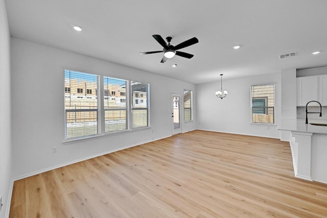 unfurnished living room featuring visible vents, recessed lighting, a sink, ceiling fan with notable chandelier, and light wood-type flooring