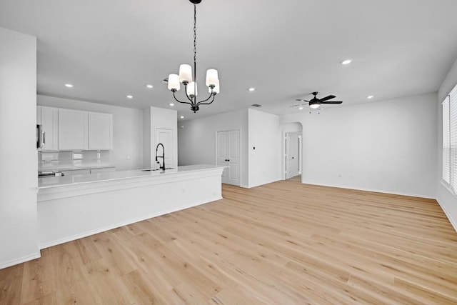 unfurnished living room featuring light wood-style flooring, ceiling fan with notable chandelier, a sink, recessed lighting, and arched walkways