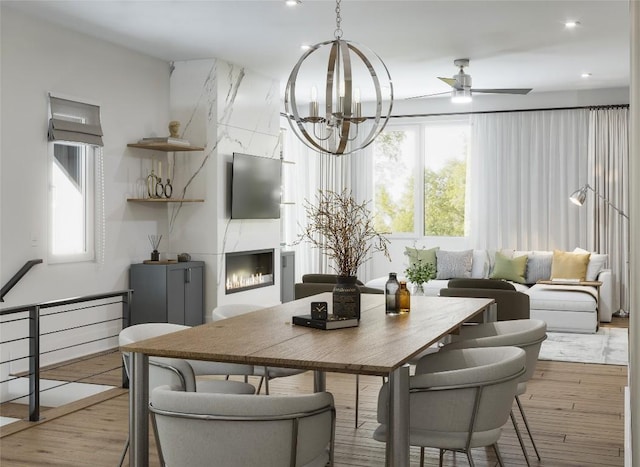 dining room with a fireplace, light hardwood / wood-style flooring, and ceiling fan with notable chandelier