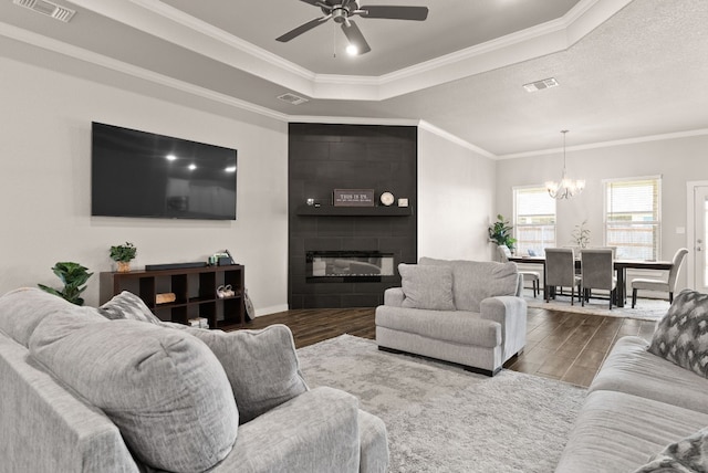 living room featuring a tile fireplace, ceiling fan with notable chandelier, ornamental molding, a textured ceiling, and a tray ceiling