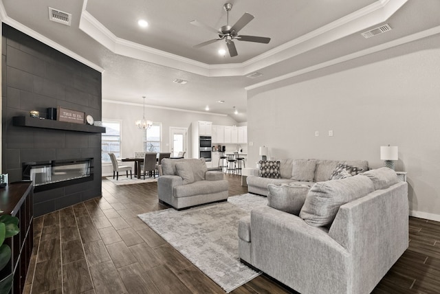 living room with a fireplace, ceiling fan with notable chandelier, a tray ceiling, and ornamental molding