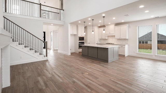 kitchen with white cabinets, stainless steel appliances, light wood finished floors, and a sink