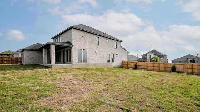 back of property featuring a lawn, a fenced backyard, and brick siding