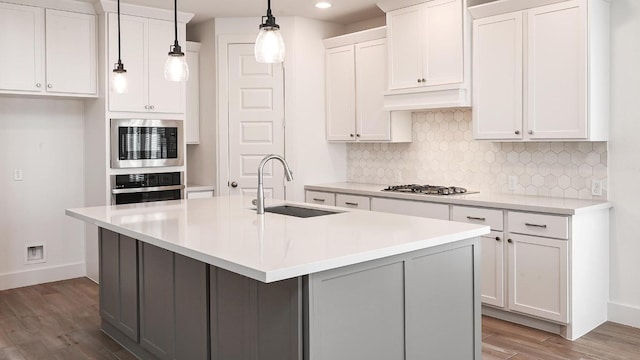 kitchen with wood finished floors, stainless steel appliances, backsplash, a sink, and baseboards