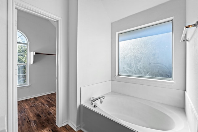 bathroom with vaulted ceiling, a tub, and hardwood / wood-style floors