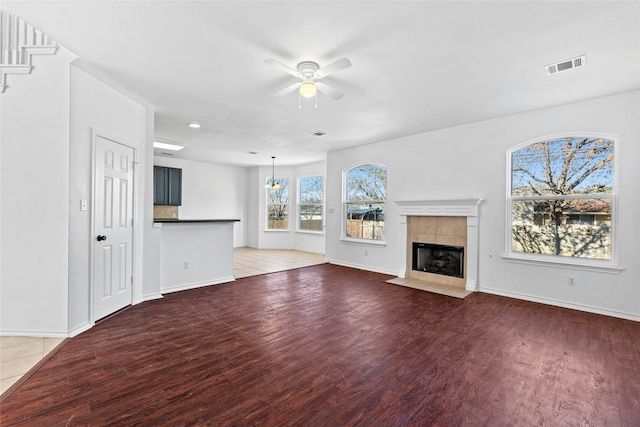 unfurnished living room with a tile fireplace, hardwood / wood-style flooring, and ceiling fan with notable chandelier