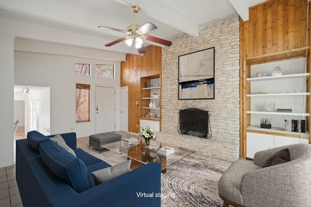 living room with tile patterned floors, a fireplace, ceiling fan, beamed ceiling, and wood walls