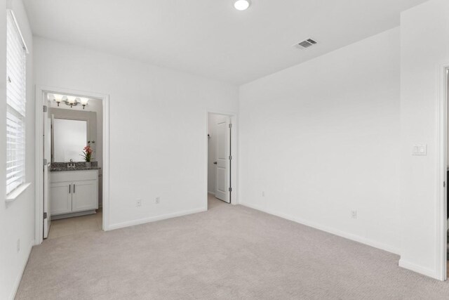 unfurnished bedroom featuring light carpet, ensuite bathroom, and multiple windows