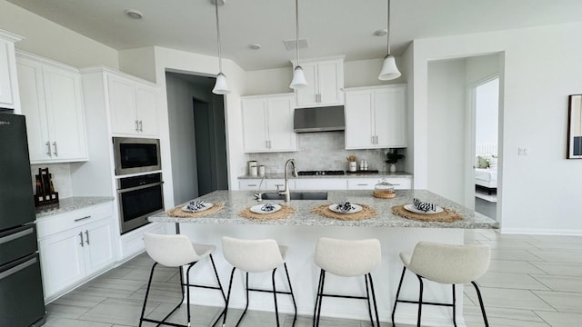 kitchen featuring stainless steel appliances, sink, a center island with sink, white cabinetry, and hanging light fixtures