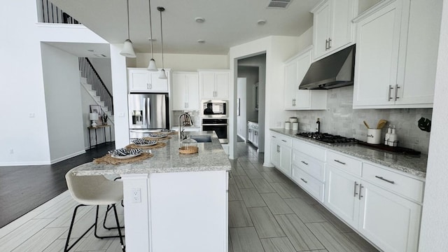 kitchen featuring light stone countertops, appliances with stainless steel finishes, tasteful backsplash, a kitchen island with sink, and white cabinets