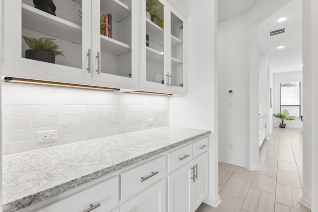 interior space featuring white cabinets, backsplash, light stone counters, and light tile patterned flooring